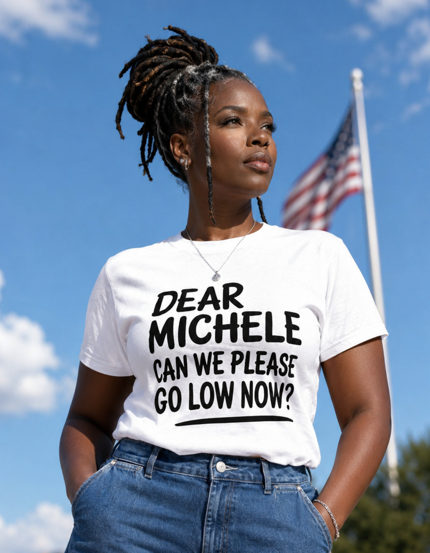 Beautiful African American woman wearing the Dear Michele graphic t-shirt with wide leg blue jeans under a blue sky with the American flag in the background.