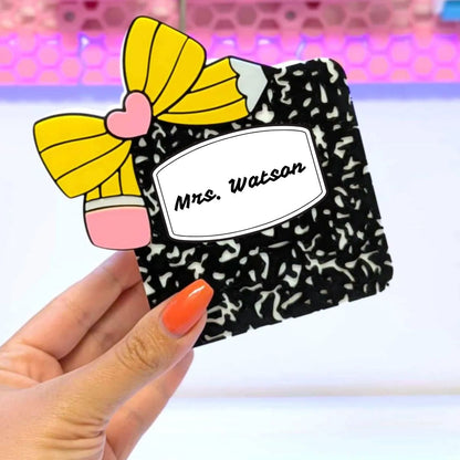 Black patterned pouch with yellow bow and 'Mrs. Watson' label held by a hand.