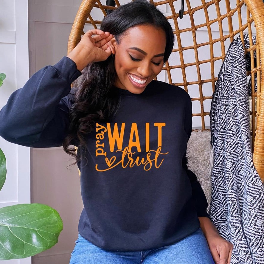Pray Wait Trust in orange font graphic sweater in navy blue featuring African American woman