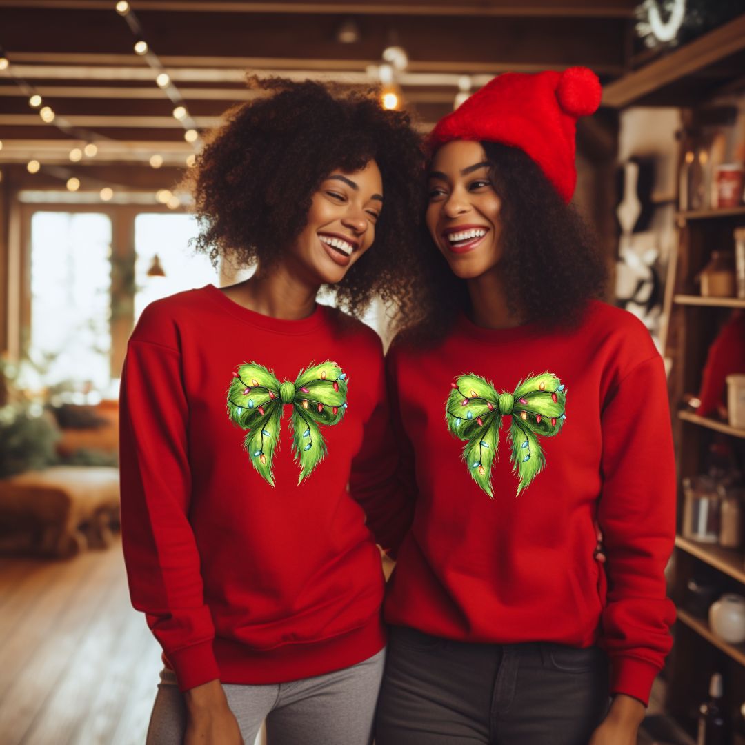 Two African American women wearing the Grinch coquette bow crewneck sweaters in red