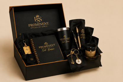 A luxury gift set from Prominent Styles of Sorts in a black presentation box. The set includes a black notebook, a black tumbler, a black candle, a gold pen, a gold pocket watch keychain, and a gold bottle keychain, all featuring the brand's gold logo on black packaging.